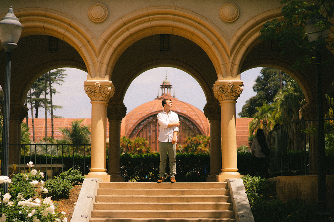 Man in white button-up shirt stands under Spanish archway at top of stairs