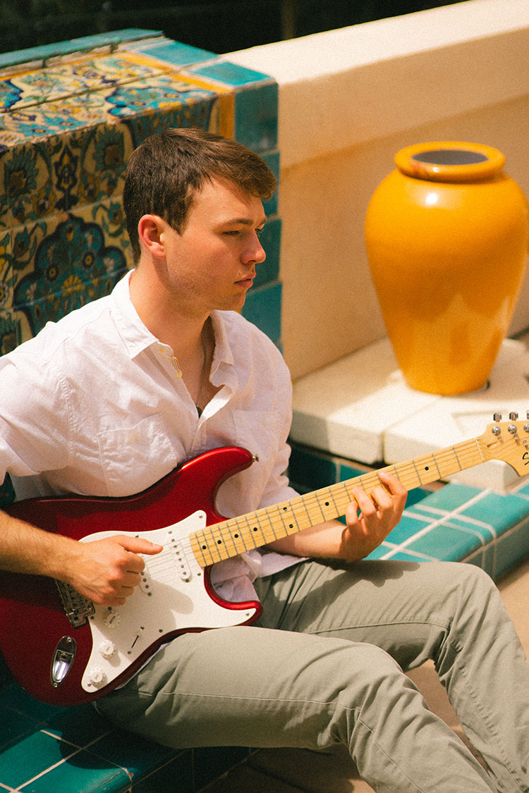 Man in white button-up shirt plays electric guitar in front of a Spanish tile fountain